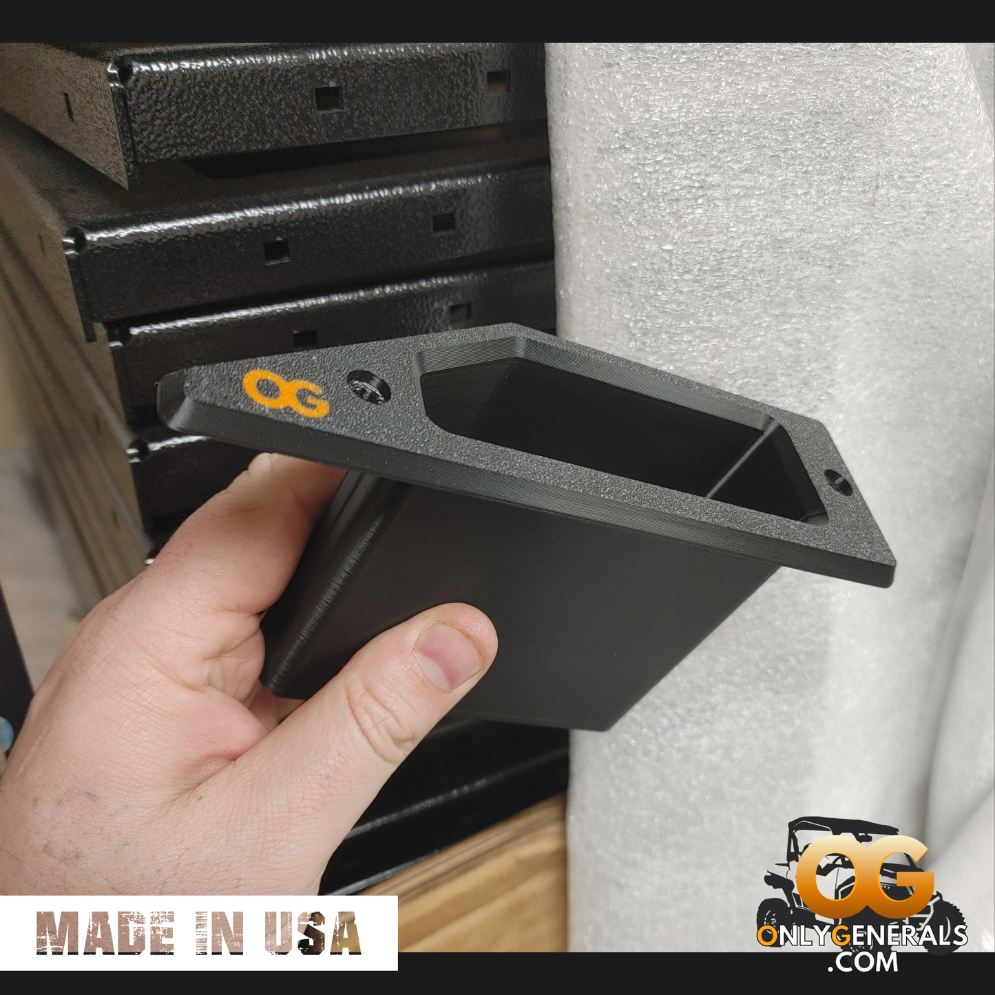 A close up photo of the OnlyGenerals recessed door pull being held by a hand in front of a stack of VersaRak frames, for the Polaris General.  Notated by the OG logo and a made in USA tag.